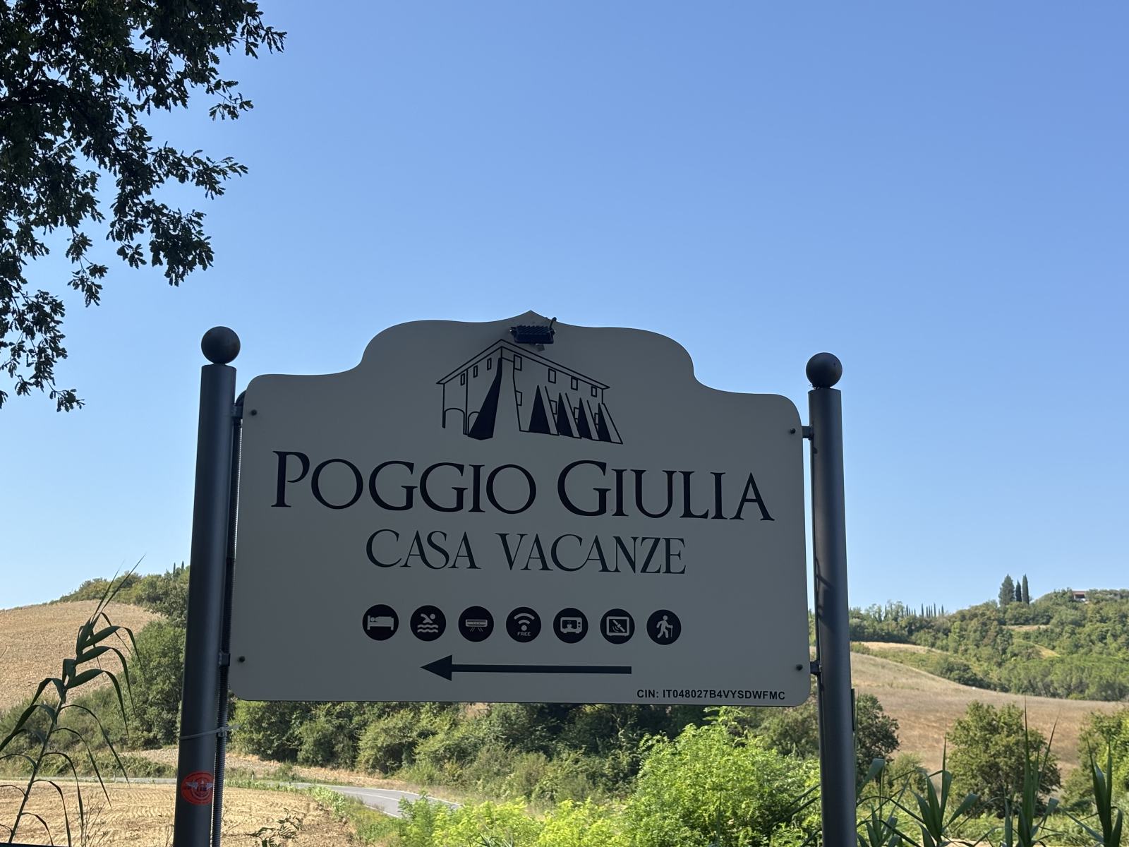 Schild 'Poggio Giulia Casa Vacanze' vor toskanischer Landschaft