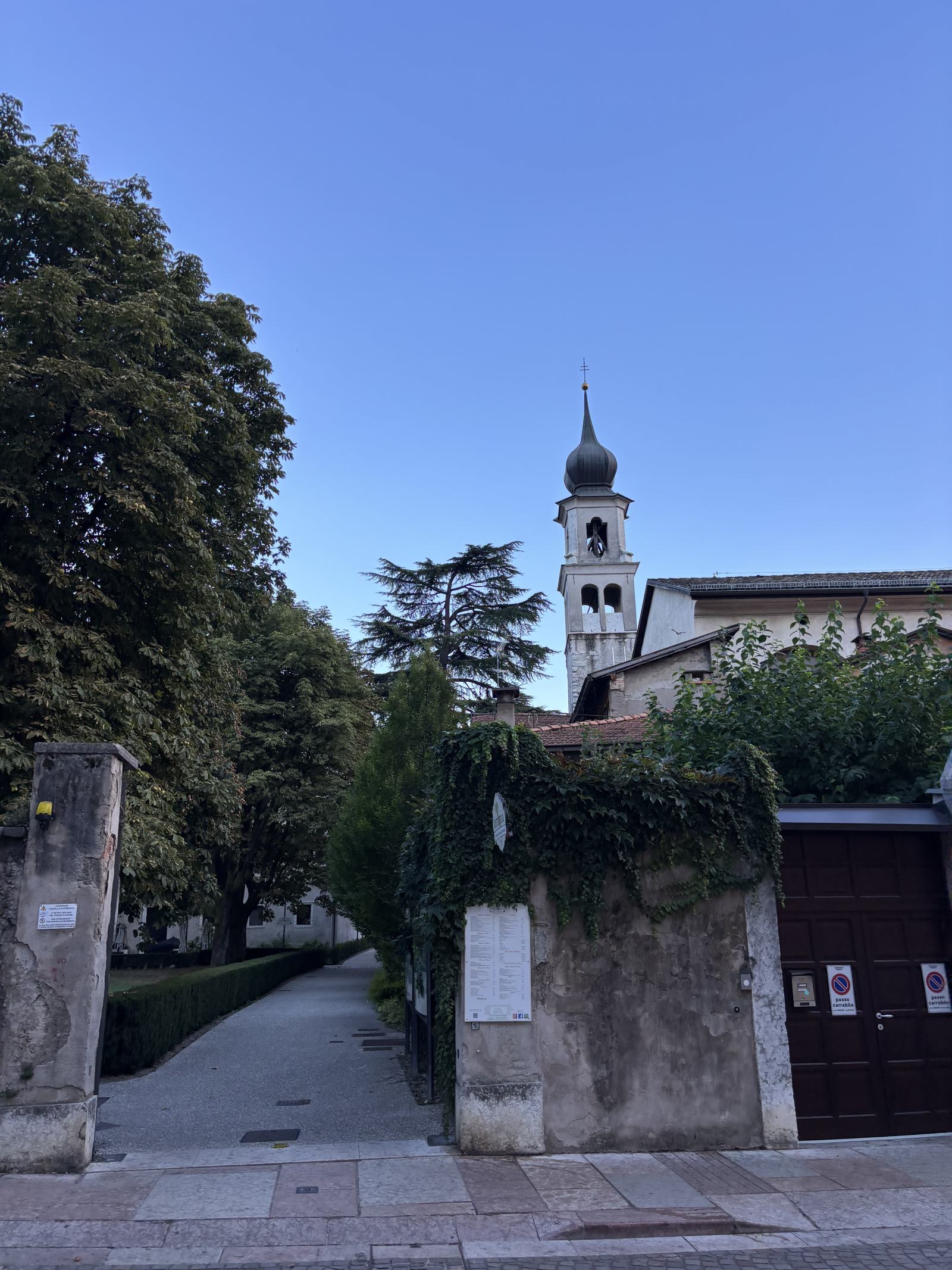 Historischer Weg mit alten Mauern und Bäumen, im Hintergrund ein Kirchturm