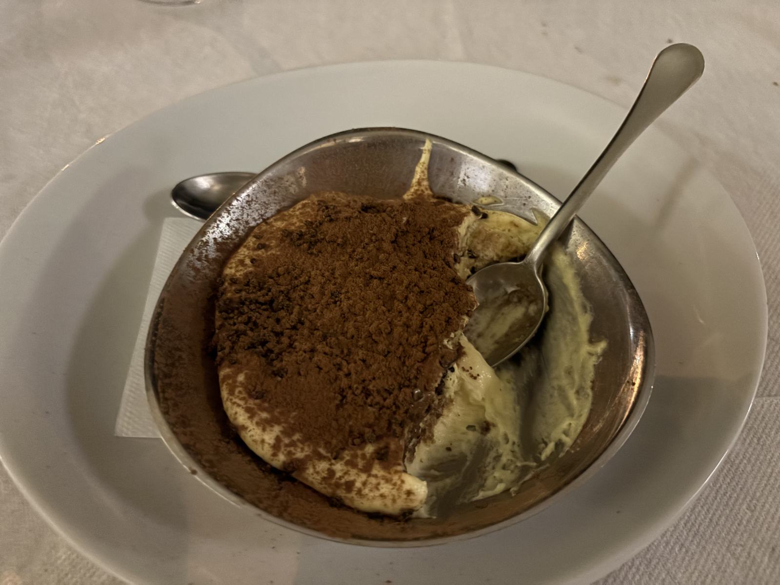 Tiramisu mit Kakaopulver in einer Metallschale, ein Löffel steckt darin.