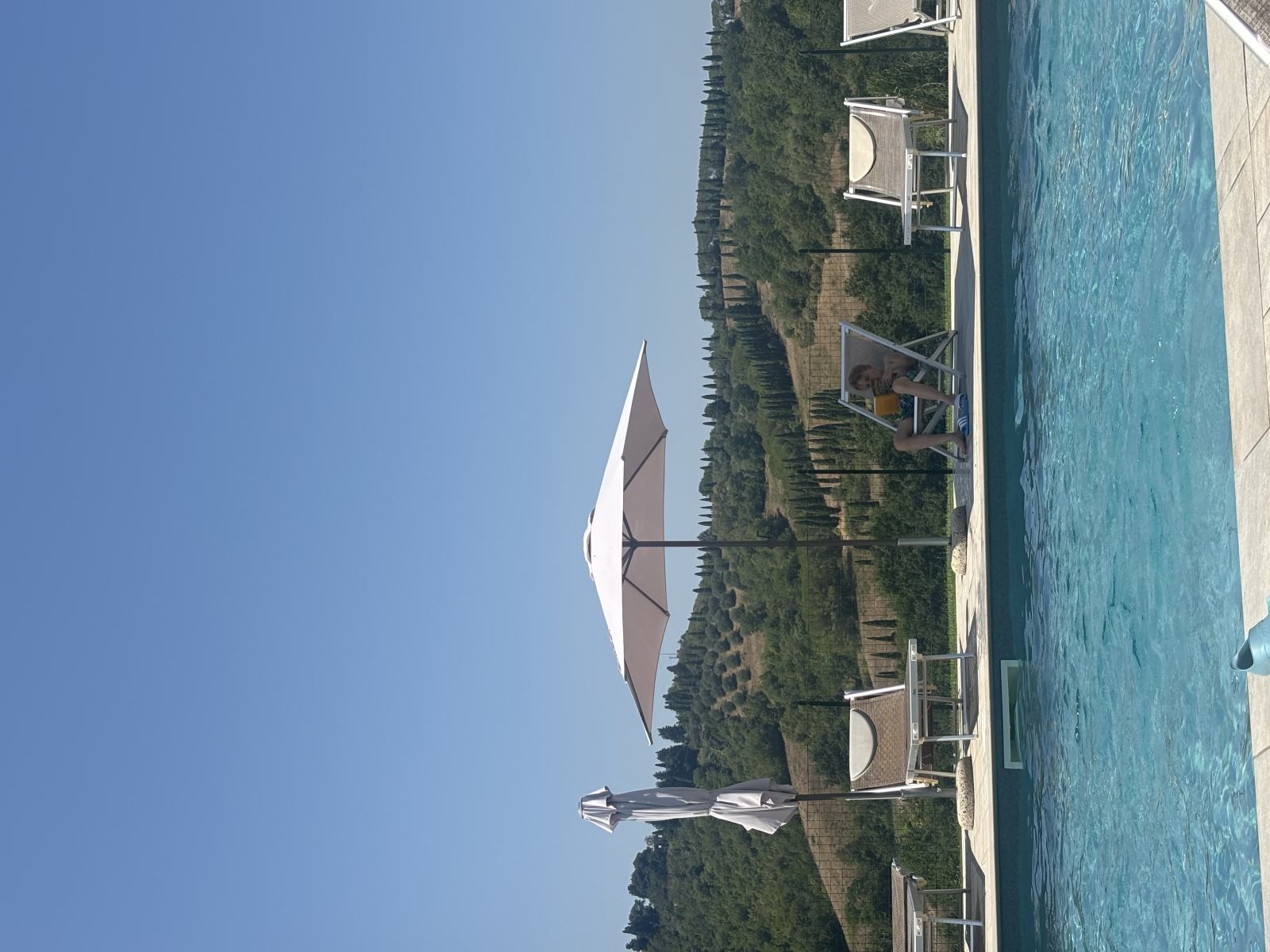 Familie am Pool in der Toskana unter strahlend blauem Himmel.